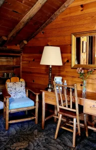 A cozy wooden room with a desk, chair, lamp, and mirror.